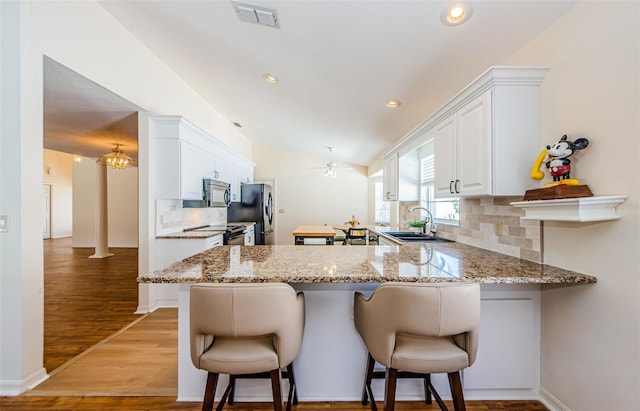 kitchen featuring a kitchen bar, visible vents, a sink, stainless steel appliances, and white cabinets