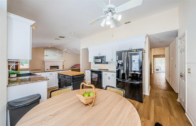 dining area with visible vents, a fireplace, ceiling fan, vaulted ceiling, and light wood-style floors