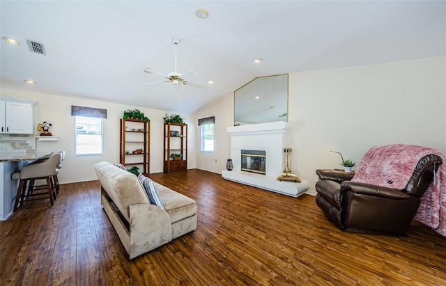 living area featuring a wealth of natural light, visible vents, vaulted ceiling, and dark wood-style flooring