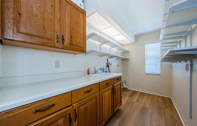 kitchen with brown cabinets, a sink, wood finished floors, light countertops, and baseboards