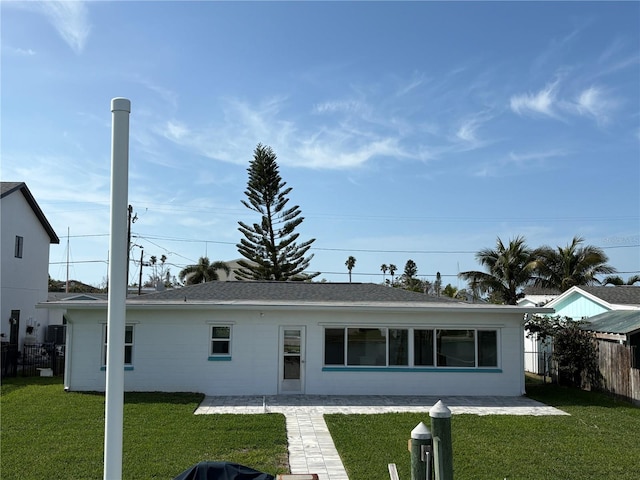 back of house with concrete block siding, roof with shingles, a patio, a lawn, and fence