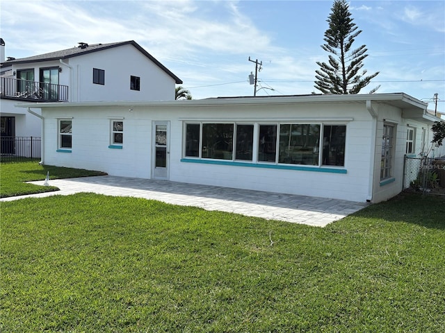 rear view of property featuring fence, concrete block siding, a patio, and a yard