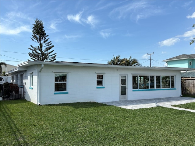 rear view of property with concrete block siding, fence, a patio, and a lawn