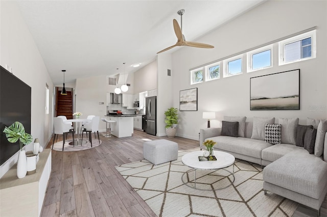 living room featuring visible vents, baseboards, ceiling fan, light wood-style floors, and high vaulted ceiling