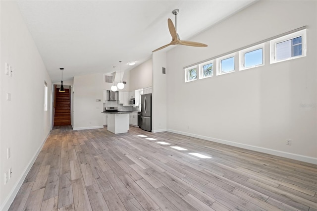 unfurnished living room featuring baseboards, ceiling fan, high vaulted ceiling, and light wood-style floors