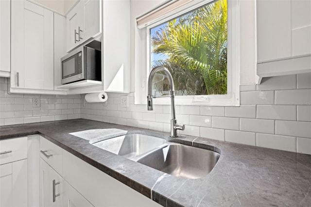 kitchen featuring a sink, stainless steel microwave, dark countertops, and white cabinets