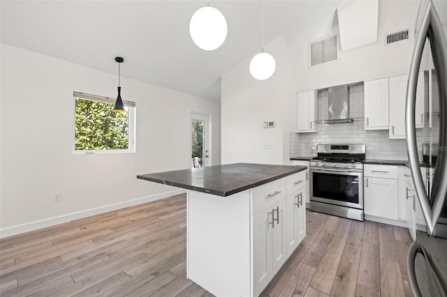 kitchen with stainless steel appliances, dark countertops, visible vents, and wall chimney range hood