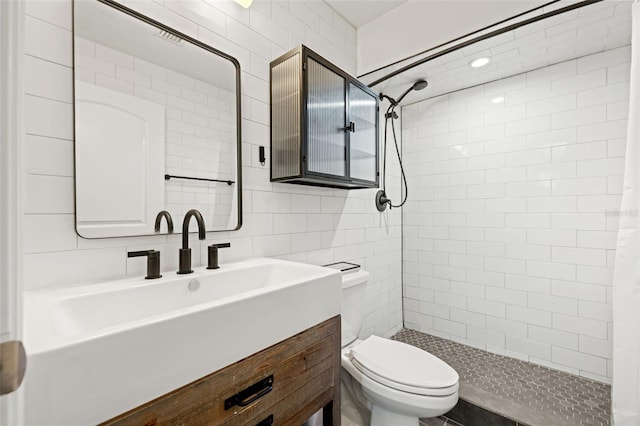 bathroom with vanity, tile walls, toilet, and a tile shower