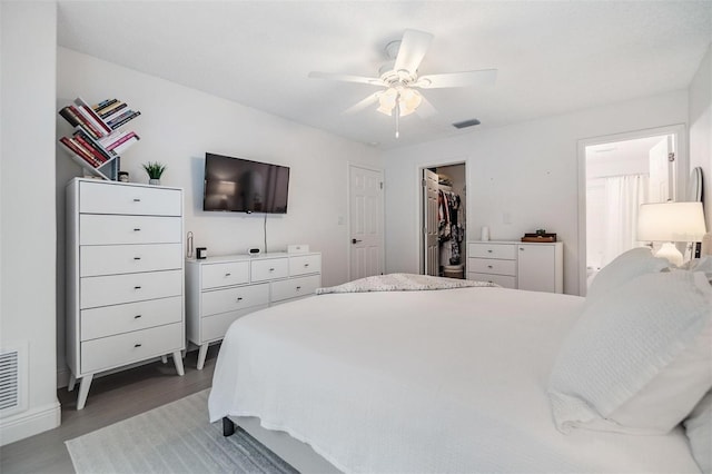 bedroom with a walk in closet, a closet, visible vents, ceiling fan, and wood finished floors