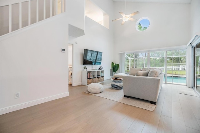 living area featuring a high ceiling, ceiling fan, baseboards, and wood finished floors