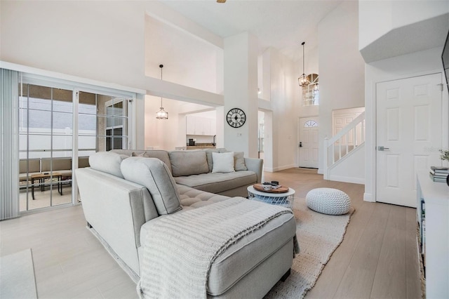 living room featuring a high ceiling, an inviting chandelier, light wood-style floors, baseboards, and stairs