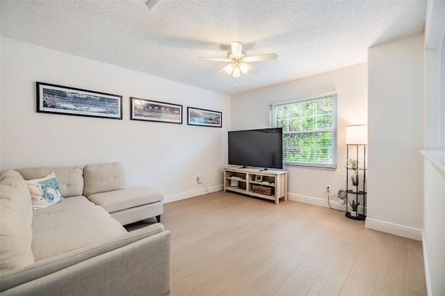 living area featuring light wood-style floors, ceiling fan, baseboards, and a textured ceiling