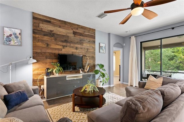 living room with arched walkways, a textured ceiling, visible vents, and tile patterned floors