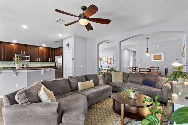 living area featuring arched walkways, ceiling fan, a textured ceiling, recessed lighting, and visible vents