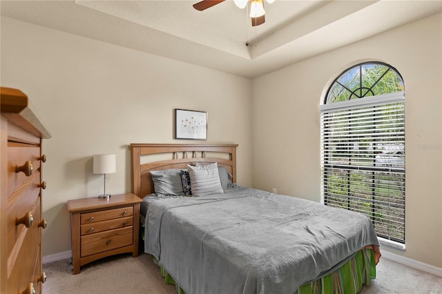 bedroom with light carpet, ceiling fan, a raised ceiling, and baseboards