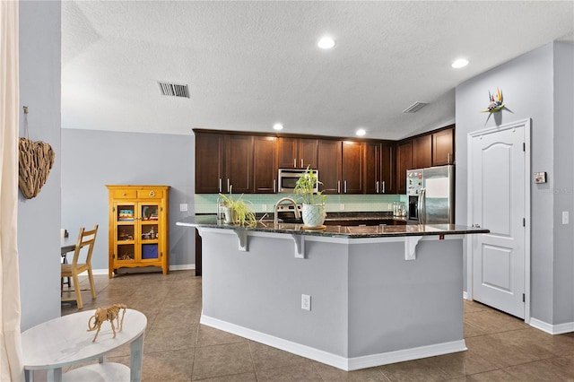 kitchen featuring appliances with stainless steel finishes, visible vents, a kitchen breakfast bar, and tasteful backsplash