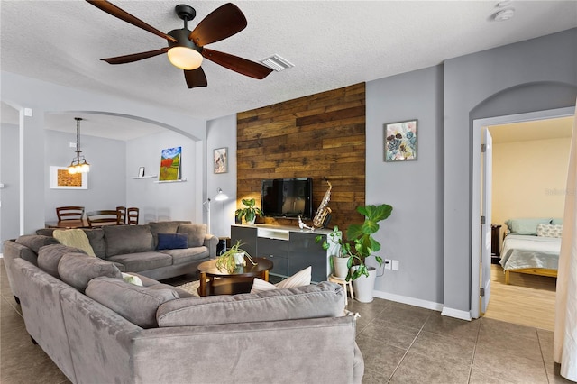 living area with wooden walls, visible vents, a ceiling fan, tile patterned flooring, and a textured ceiling