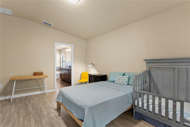 bedroom with visible vents, vaulted ceiling, baseboards, and wood finished floors