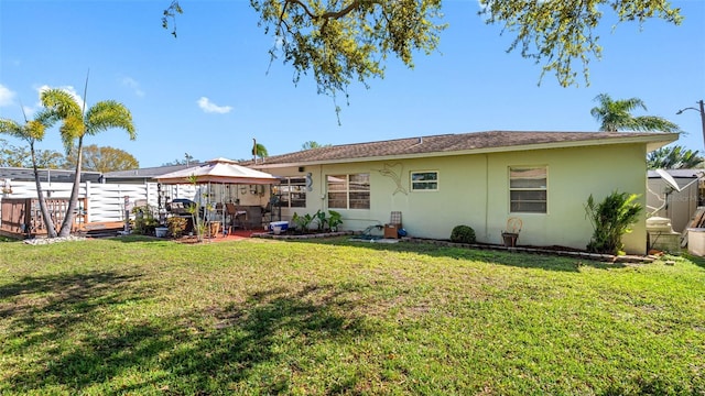 back of property featuring a lawn, fence, a gazebo, a patio area, and stucco siding