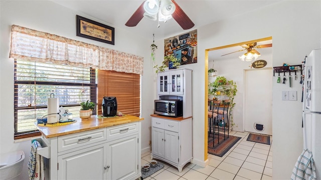 kitchen featuring light tile patterned floors, ceiling fan, stainless steel microwave, freestanding refrigerator, and white cabinetry