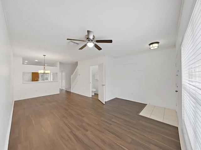 unfurnished living room with dark wood-style floors, visible vents, ceiling fan, and stairway