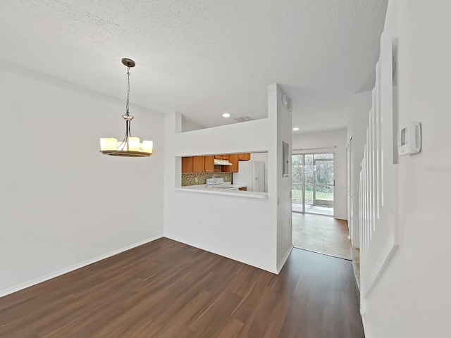 empty room with a notable chandelier, a textured ceiling, dark wood-type flooring, and recessed lighting