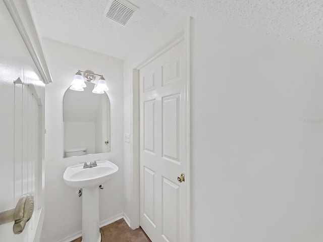 bathroom with visible vents, a textured ceiling, and baseboards