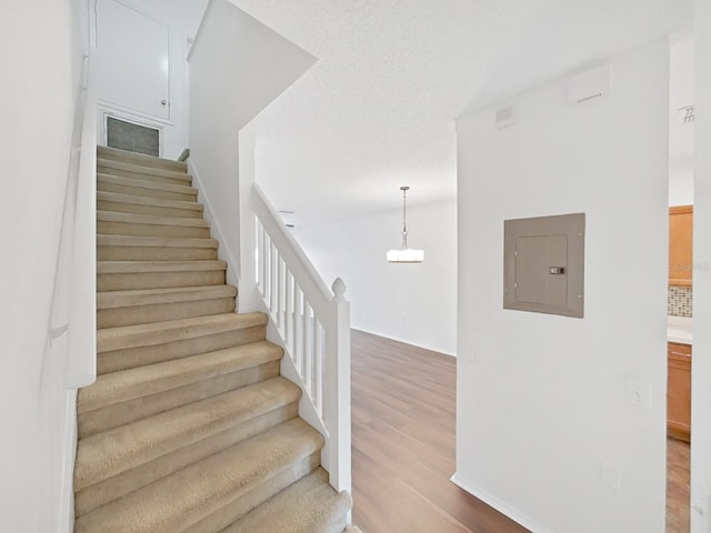 stairs featuring a chandelier, electric panel, visible vents, and wood finished floors