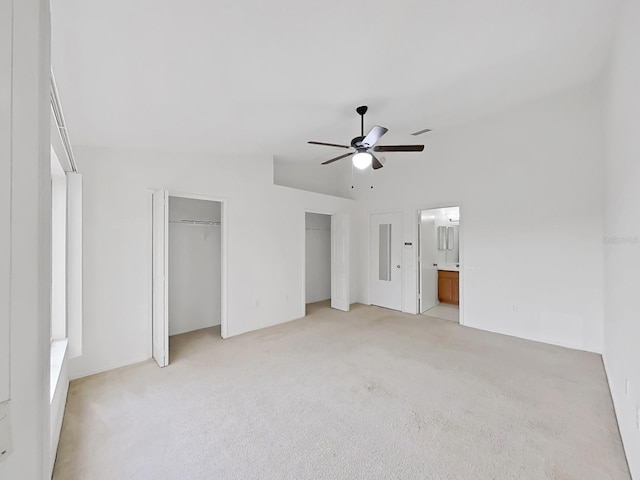 unfurnished bedroom with two closets, ensuite bathroom, a ceiling fan, light carpet, and vaulted ceiling