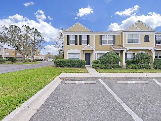 townhome / multi-family property featuring uncovered parking, a front yard, a residential view, and stucco siding