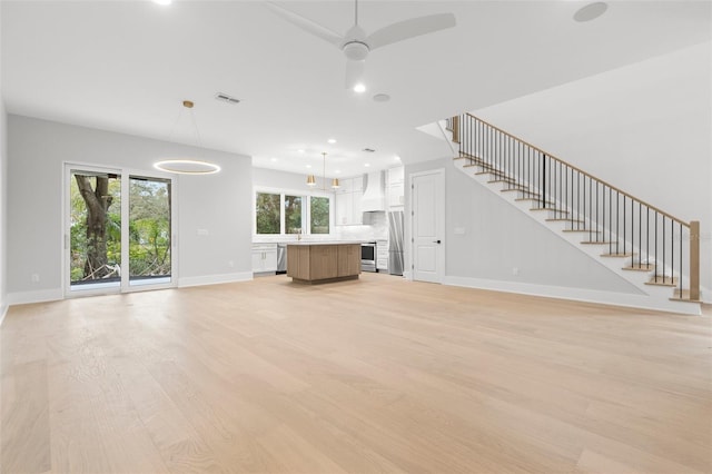 unfurnished living room with light wood finished floors, visible vents, baseboards, ceiling fan, and stairway