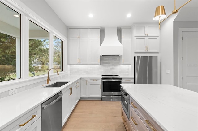 kitchen with light wood finished floors, custom range hood, appliances with stainless steel finishes, a sink, and backsplash