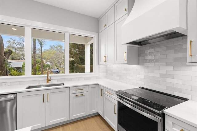 kitchen featuring stainless steel appliances, light countertops, backsplash, a sink, and wall chimney exhaust hood