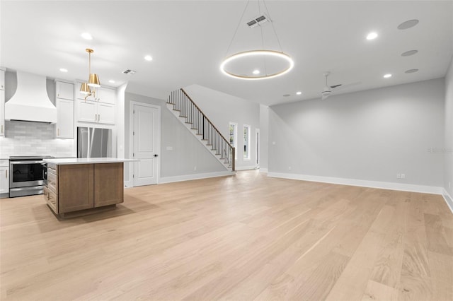 kitchen with a center island, light wood finished floors, stainless steel appliances, custom range hood, and backsplash