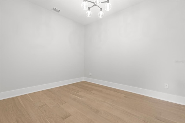 spare room featuring a chandelier, baseboards, visible vents, and light wood-style floors