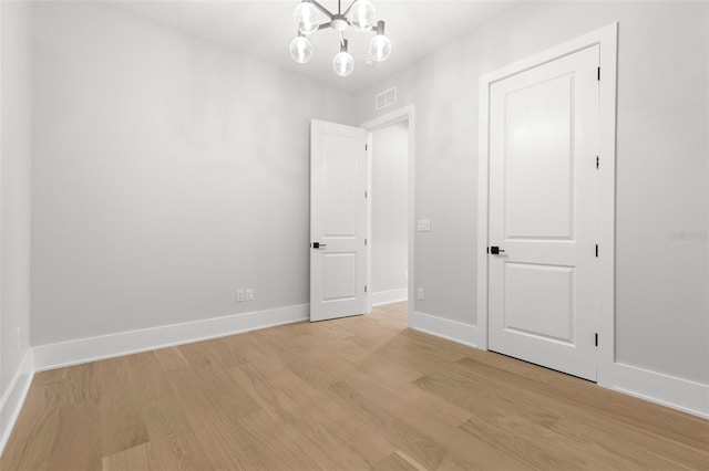 unfurnished room with a notable chandelier, light wood-style flooring, visible vents, and baseboards