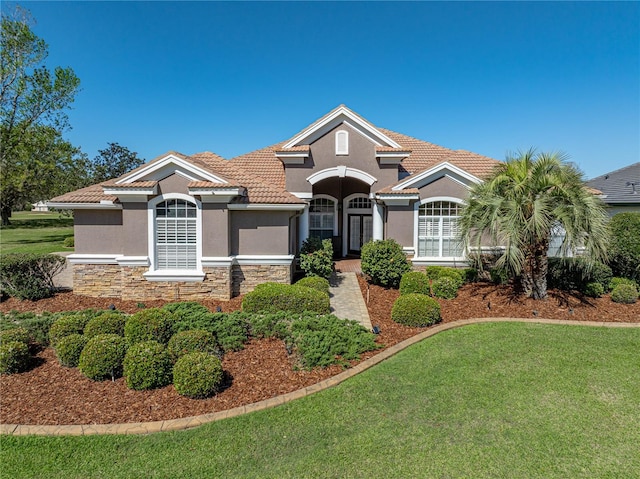 mediterranean / spanish-style house featuring stone siding, a front lawn, stucco siding, and a tiled roof