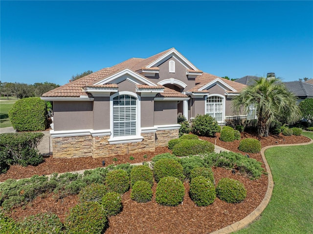 mediterranean / spanish-style home featuring stone siding, a front yard, a tile roof, and stucco siding