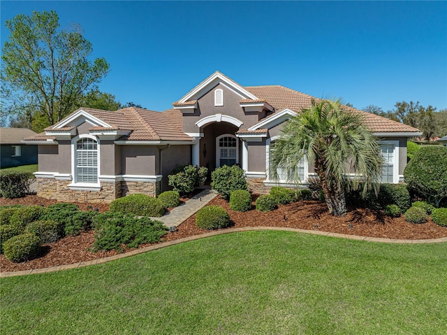 mediterranean / spanish-style house with a front yard, stone siding, a tiled roof, and stucco siding