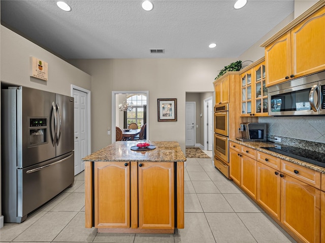 kitchen with stone counters, visible vents, appliances with stainless steel finishes, a center island, and glass insert cabinets