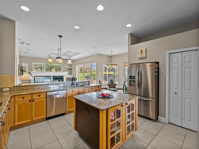 kitchen featuring appliances with stainless steel finishes, a chandelier, a sink, and light stone countertops