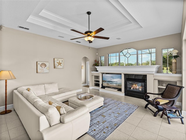 tiled living room featuring visible vents, a raised ceiling, crown molding, and a glass covered fireplace