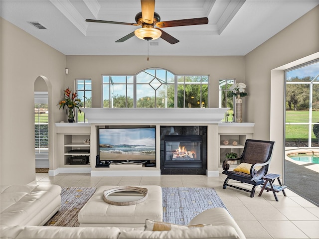 living room with a tray ceiling, a wealth of natural light, and a glass covered fireplace