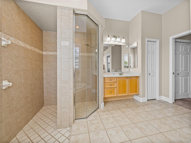 bathroom with tile patterned flooring, a tile shower, vanity, and baseboards