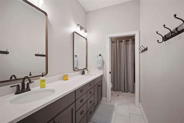 full bath with double vanity, a sink, toilet, and baseboards