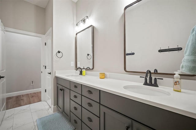 bathroom featuring marble finish floor, a sink, baseboards, and double vanity