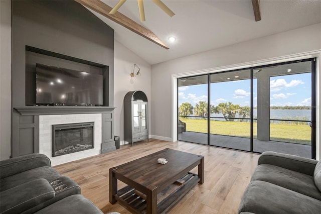 living room featuring light wood finished floors, baseboards, arched walkways, a glass covered fireplace, and beam ceiling