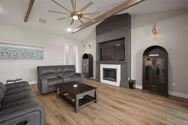 living room with baseboards, visible vents, a glass covered fireplace, lofted ceiling with beams, and light wood-style floors