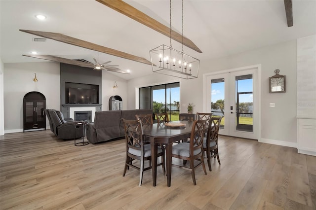 dining area featuring baseboards, visible vents, a glass covered fireplace, vaulted ceiling with beams, and light wood-style floors