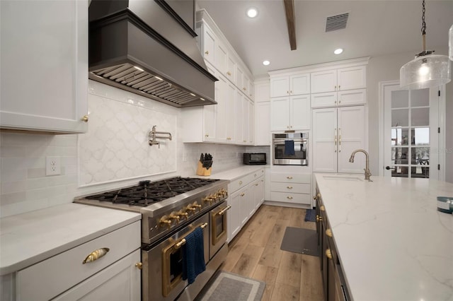 kitchen with visible vents, appliances with stainless steel finishes, custom exhaust hood, white cabinetry, and a sink